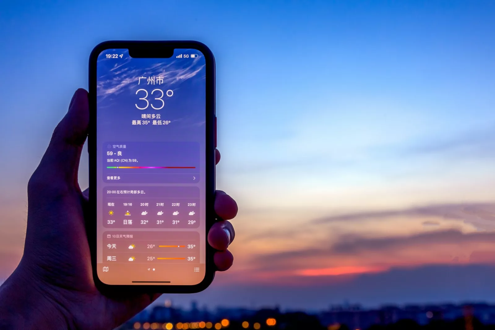 A hand holds an iPhone displaying a weather app. The screen shows a temperature of 33°C in Guangzhou, with a gradient sky transitioning from blue to orange, suggesting sunset. The image reflects the features of the A17 chip focusing on battery efficiency.